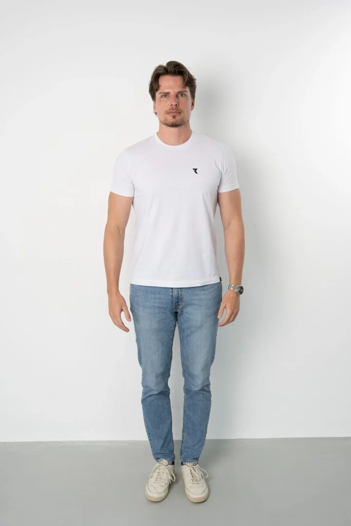 Mann im weißen T-Shirt und Jeans vor weißer Wand