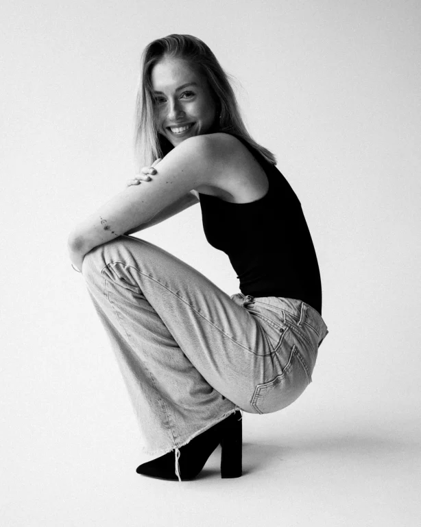 Lächelnde Frau hockt im Studio in Jeans und schwarzem Top