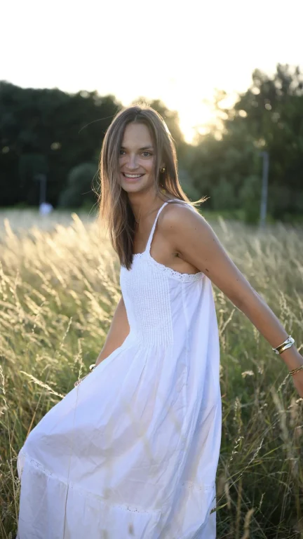 Lächelnde Frau im weißen Kleid auf sonniger Wiese