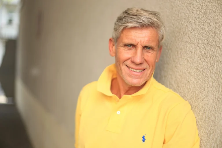 Lächelnder grauhaariger Mann im gelben Poloshirt an einer Wand