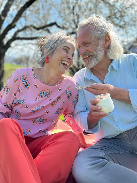 Lachendes älteres Paar genießt Joghurt unter blühendem Baum