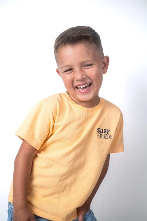 Lachender Junge im gelben T-Shirt vor weißem Hintergrund